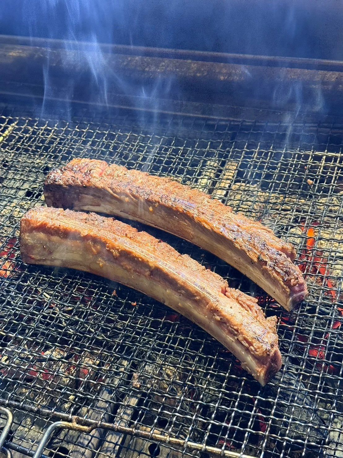 炭火の焼き網の上で薄切り肉が音を立てながら焼けている近距離の写真