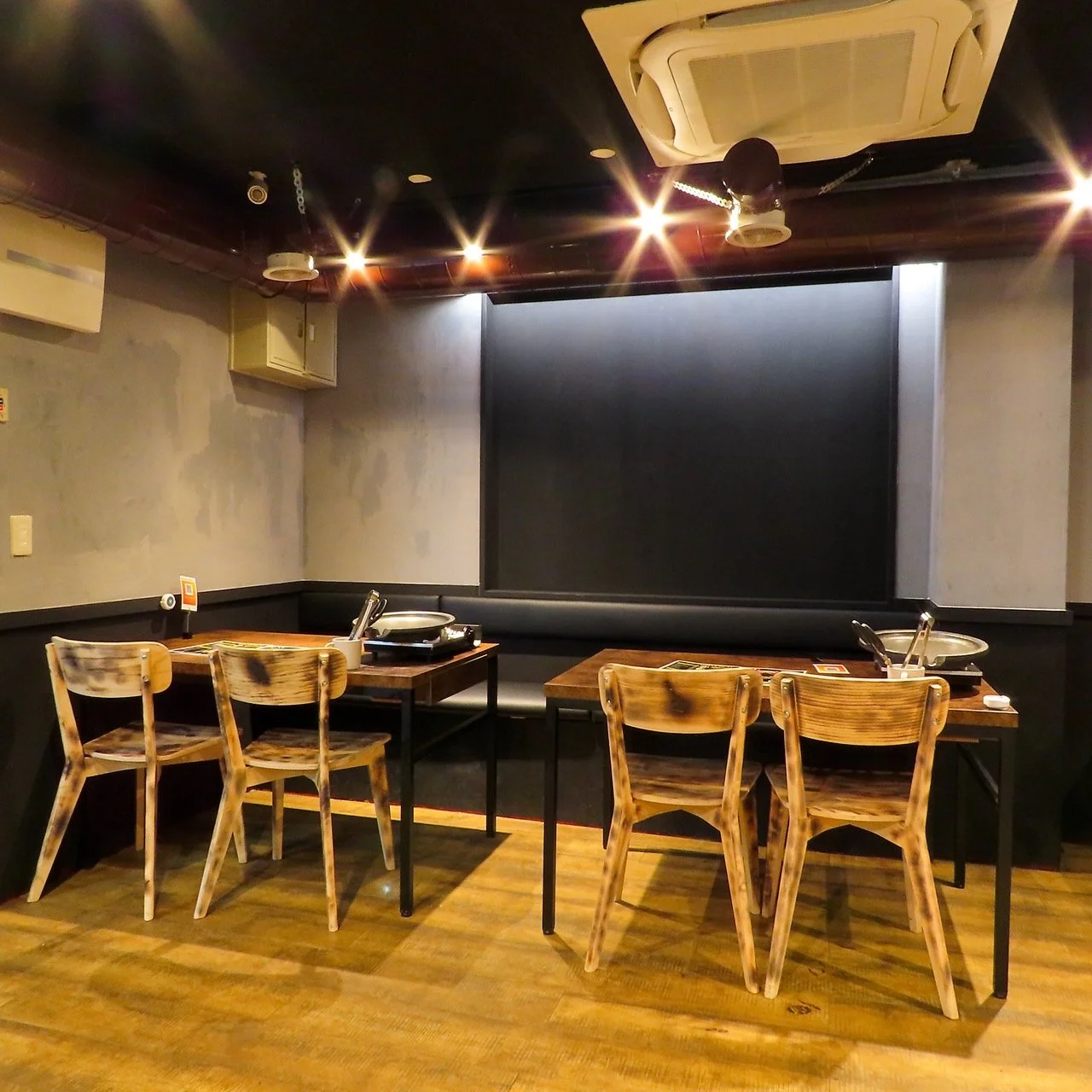 木のテーブル席と奥の照明が連なる店内を斜めから見た全景